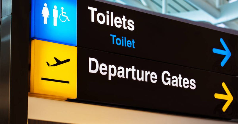 An illuminated airport sign features the words "Toilets" and "Departure Gates" with arrows pointing in the same direction.