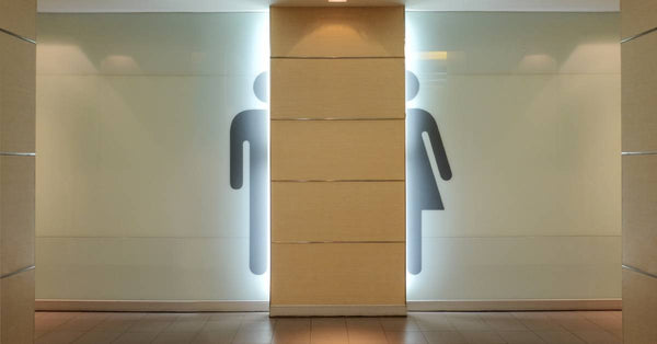 The entrance of a public bathroom features the backlit symbols for men's and women's restrooms, separating the entrances.