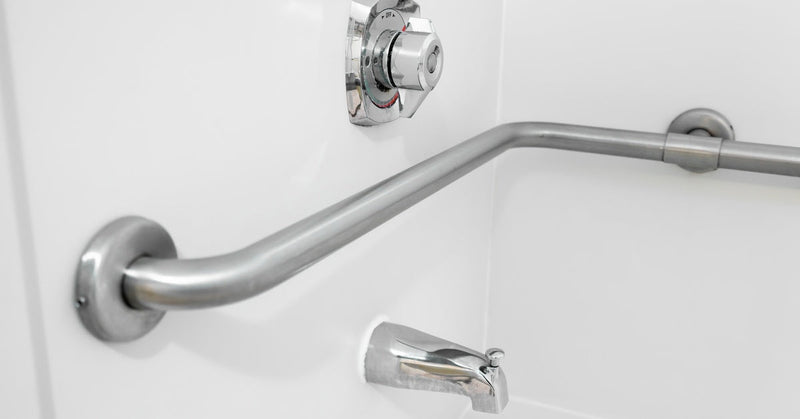 An L-shaped stainless steel grab bar is installed in a clean, white shower stall with a chrome faucet.