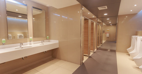 A clean public restroom features tan tile, a contrasting walkway in brown tile, and a row of white porcelain urinals.
