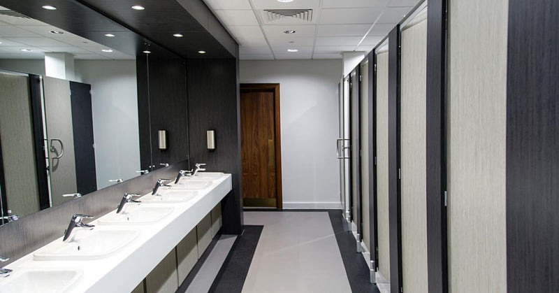 A luxury public bathroom features two toilet stalls with wood doors and two sinks with round mirrors on the wall.
