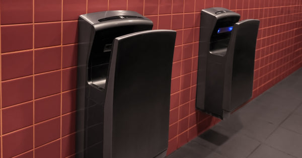 A pair of large energy-efficient wall-mounted hand dryers on the red tile wall of a public bathroom.