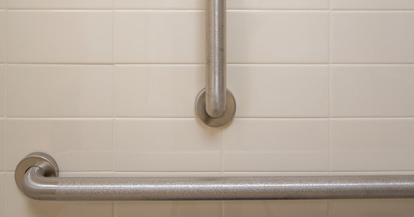 A close up of both a horizontal and vertical grab bar on a white tile wall. The bar has a textured finish on it.