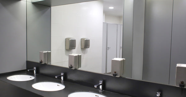 A large framed rectangular mirror attached to a tile wall above a white countertop with a pair of sinks in it.