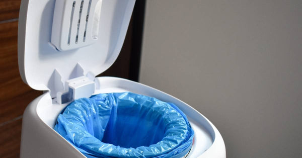 A small, white, specialized waste disposal unit with a blue bag. The lid has a visible locking mechanism on top.