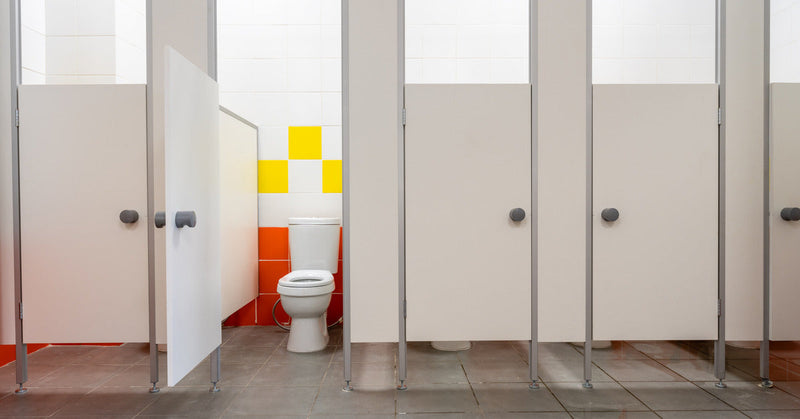 A row of closed stalls in a public bathroom. One stall door is open, revealing a clean white toilet inside.